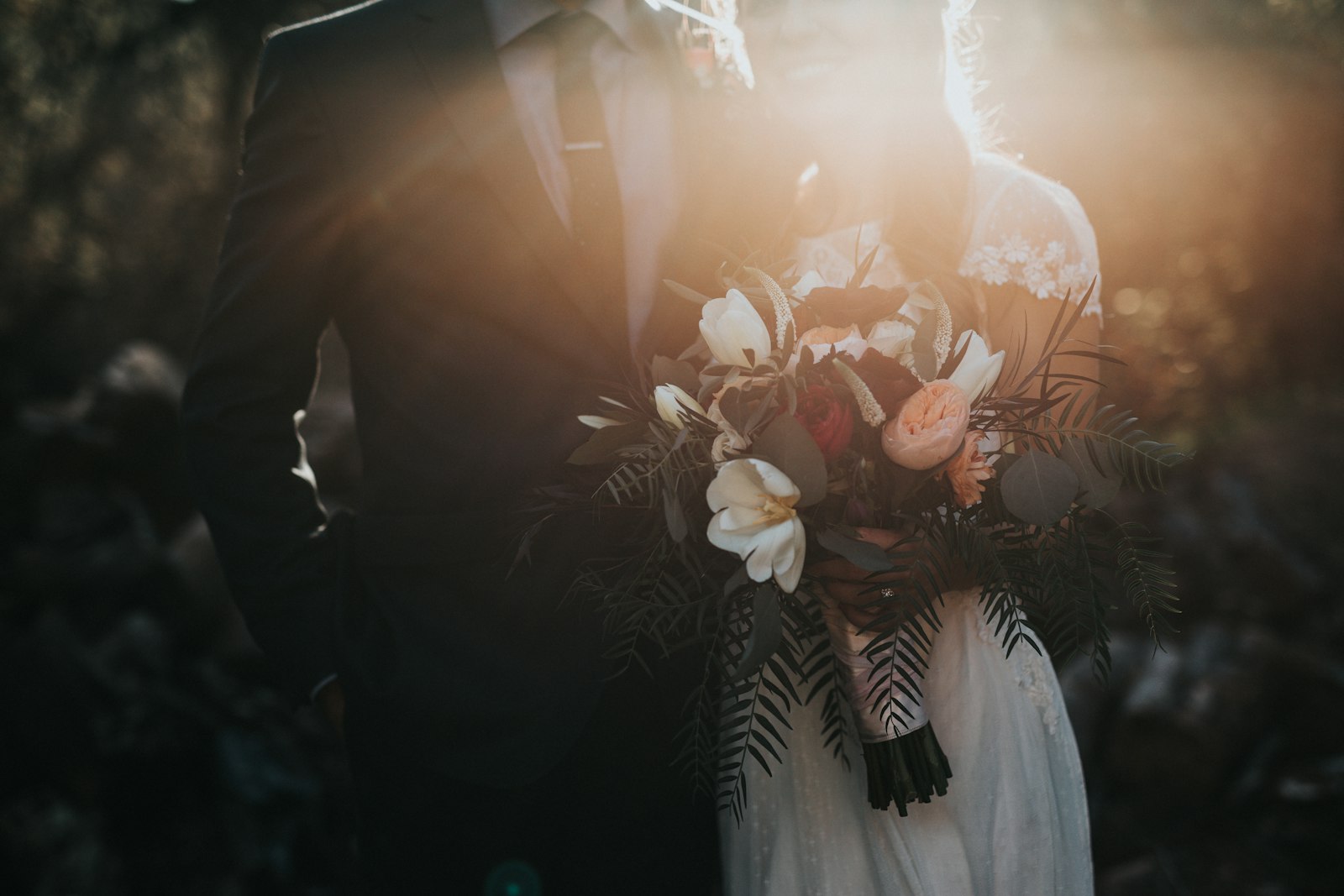 A bride holding a pale garden-style bouquet in low light